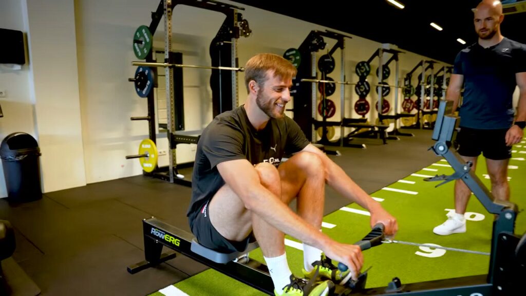 Atleet roeit op een Concept2 RowErg naast de groene trainingsbaan