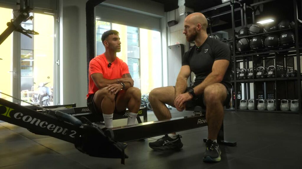 Twee atleten in gesprek op Concept2-roeitrainers in de gym