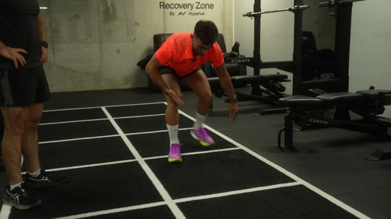 Atleet midden in een burpee broad jump op de zwarte trainingsvloer